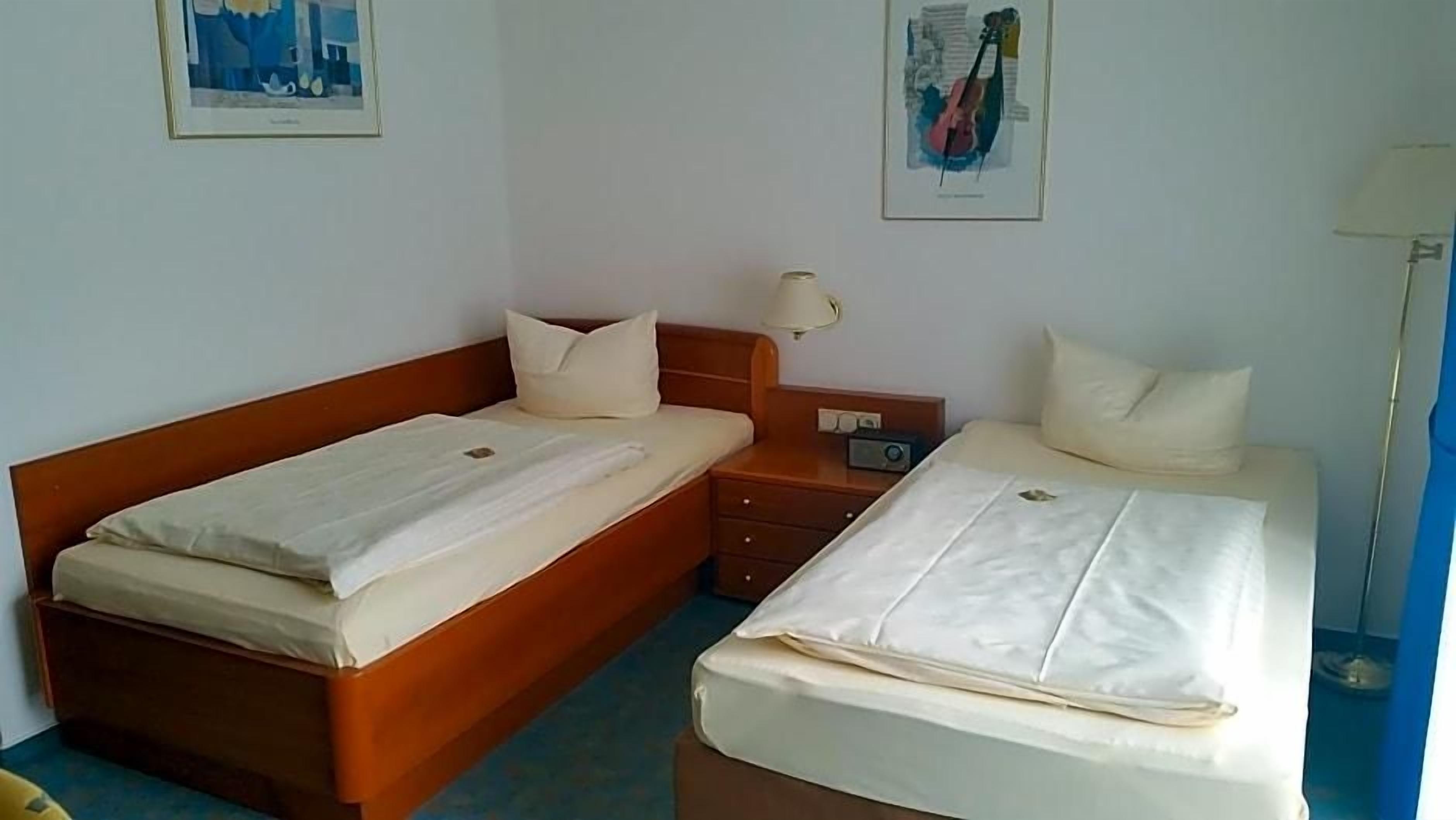 A hotel room with two beds, a bedside table with a lamp, and artwork on the walls.
