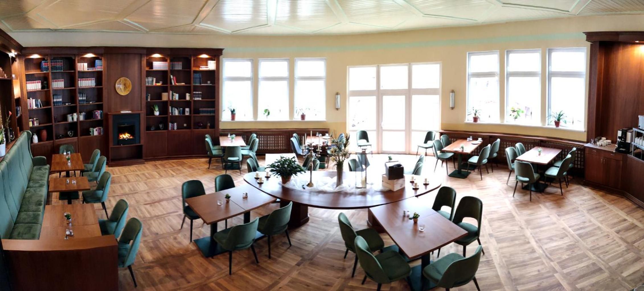 Een ruime binnenruimte met diverse zithoekjes, waaronder tafels en stoelen, omringd door boekenkasten en een open haard.