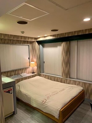 A hotel room with a bed, bedside table, lamp, and curtains.