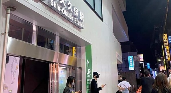 A building with a sign that reads 'Shin-Okubo Station' and a green directional arrow.