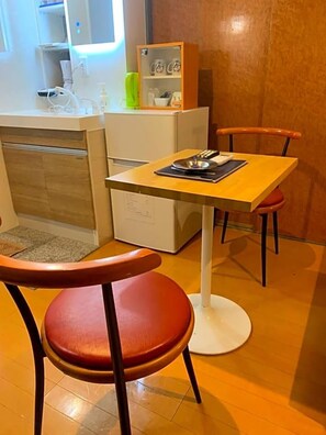 A compact kitchen with a dining area, including a table and chairs, and a small refrigerator.