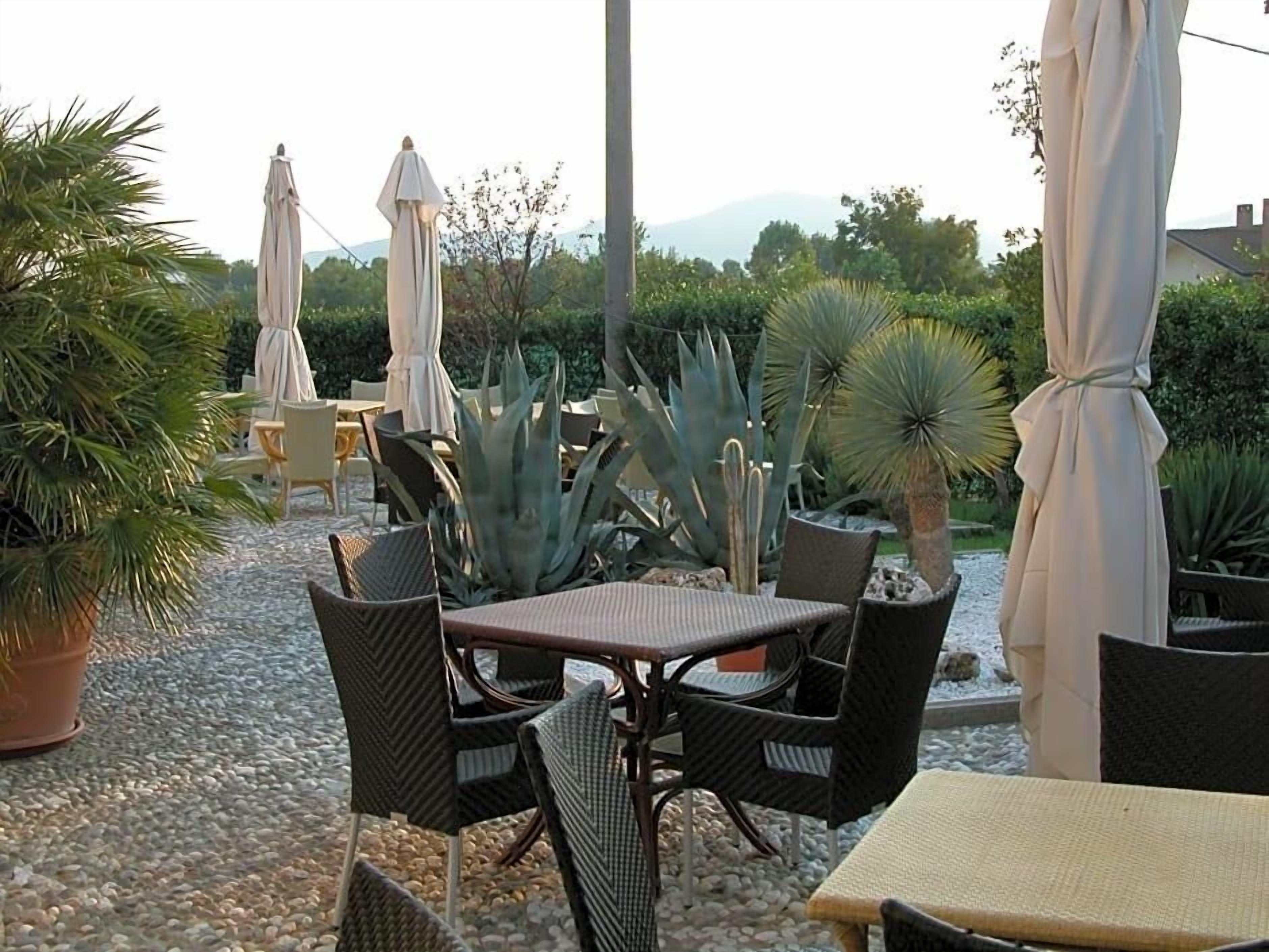 Eine Terrassengaststätte mit Tischen und Stühlen, umgeben von Blumentöpfen und Sonnenschirmen.