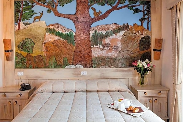 A bedroom with a large mural of a forest scene, a bed with a tray of breakfast, and bedside tables with lamps. - Garnv La Rua Nel Bosco (Rivisondoli)