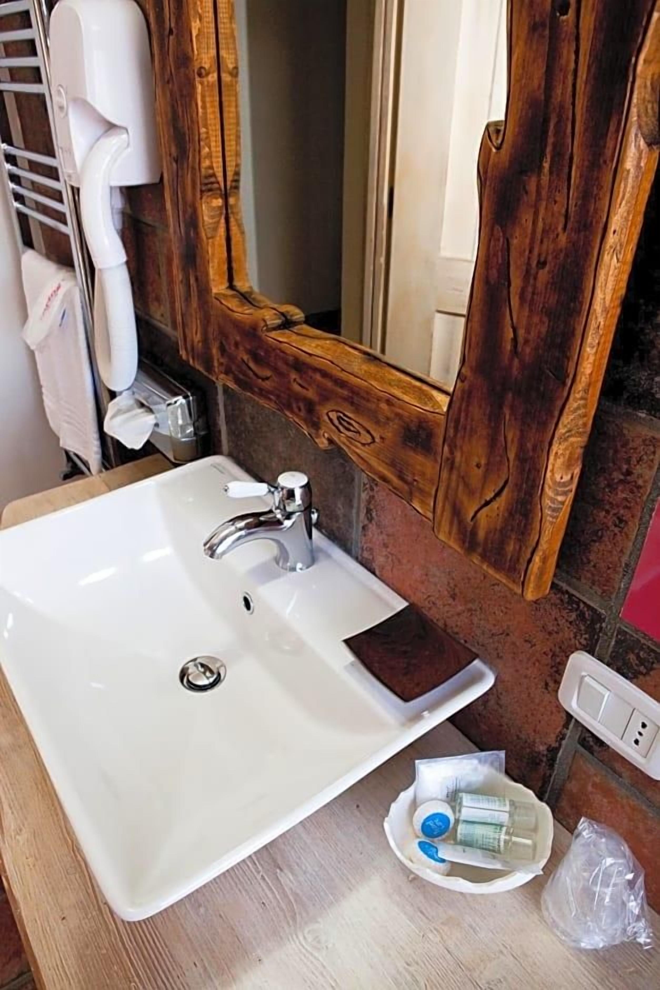 Un bagno con un lavandino bianco, uno specchio con cornice in legno e articoli da toilette sul ripiano.
