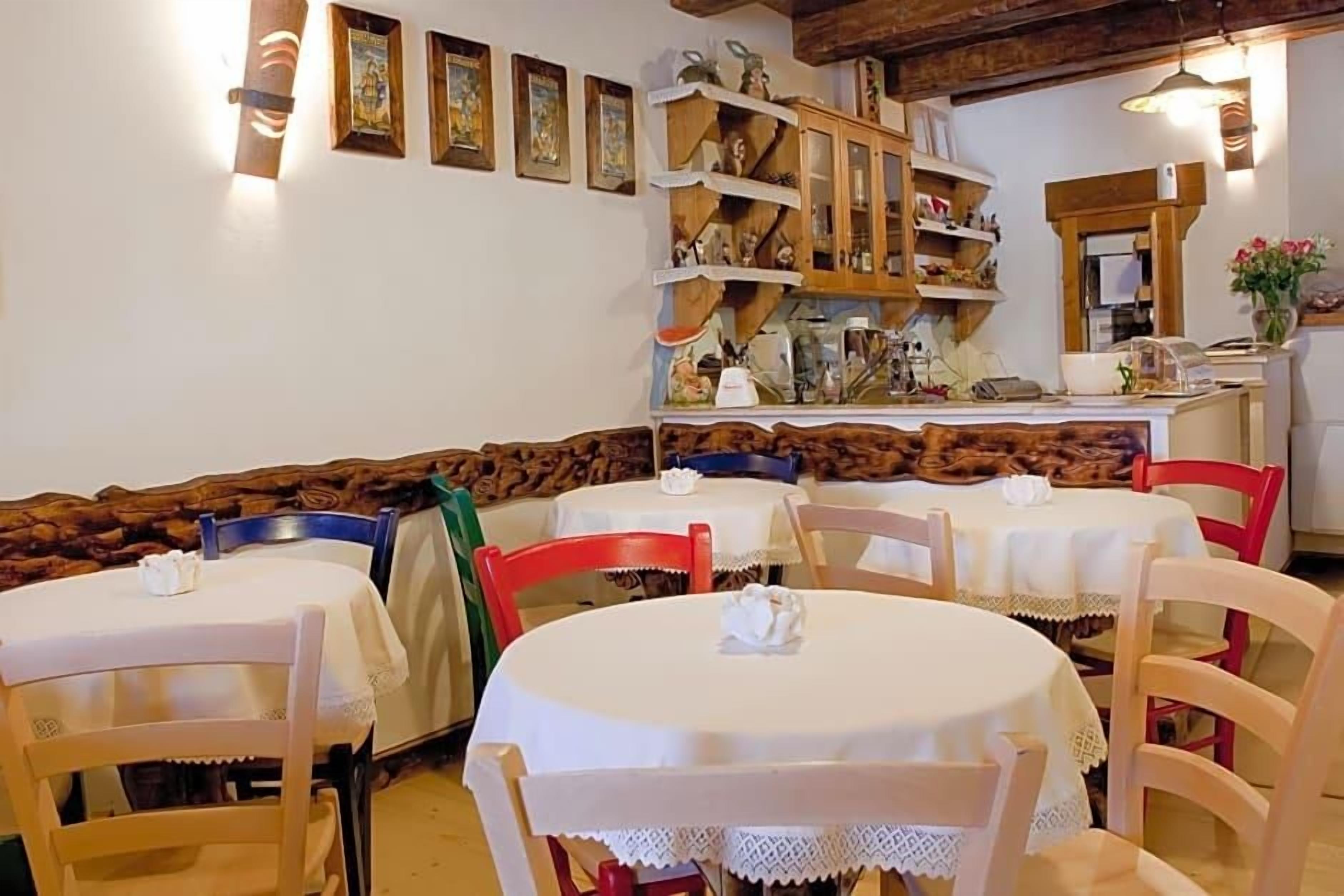 Zona pranzo con tavoli e sedie rotonde, una panca in legno ed elementi esposti su mensole a parete.