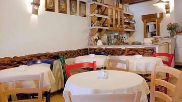 Zona pranzo con tavoli e sedie rotonde, una panca in legno ed elementi esposti su mensole a parete.