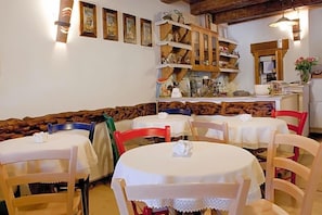 A dining area with round tables and chairs, a wooden bench, and wall-mounted shelves with various items. - Garnv La Rua Nel Bosco (Rivisondoli)
