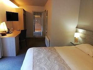 A hotel room with a bed, a desk with a chair, a television mounted on the wall, and a door leading to another room. - Hotel Le Lv Man (Saint-Gingolph)