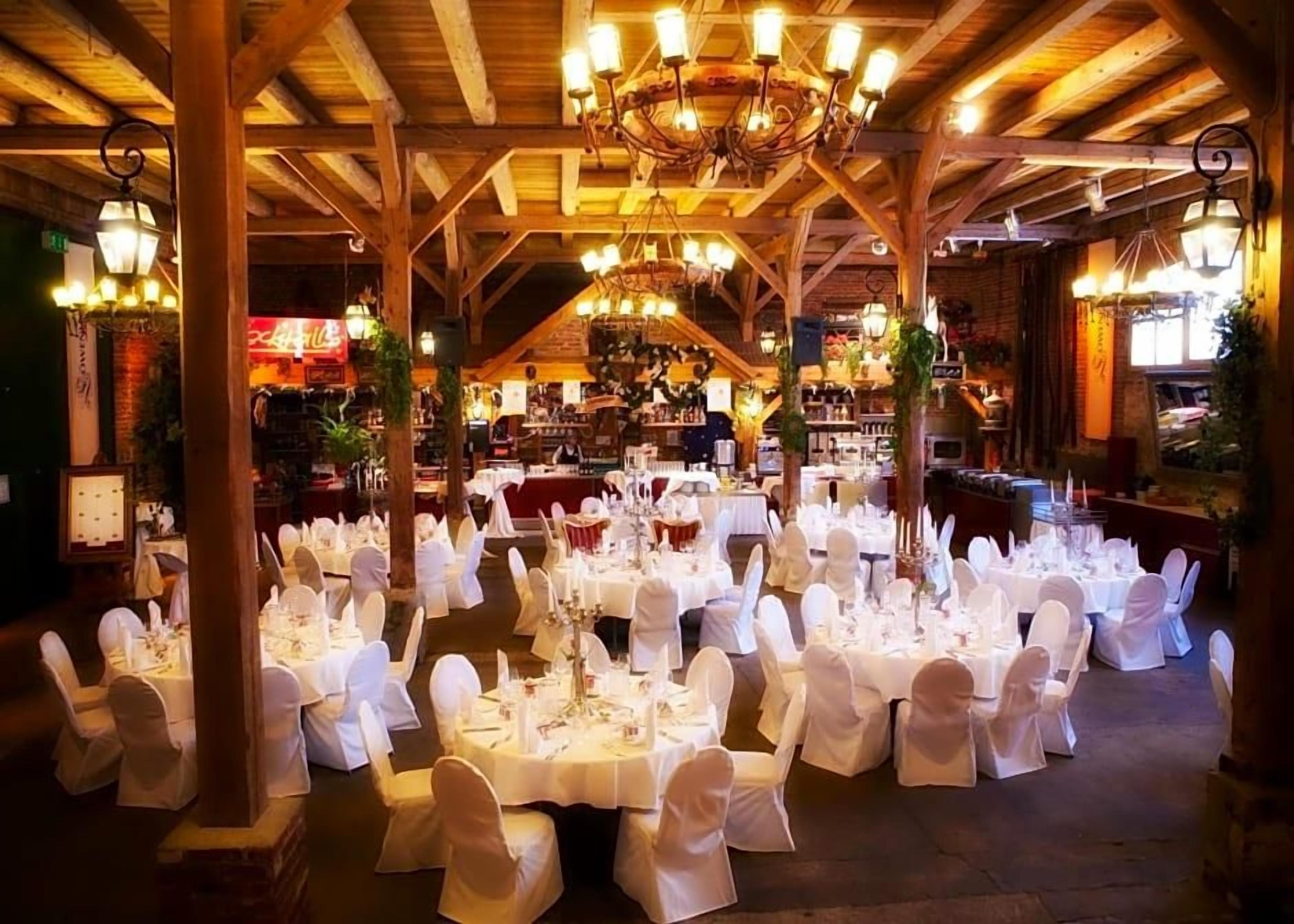 A banquet hall with round tables set for a formal event, wooden beams on the ceiling, and hanging light fixtures.