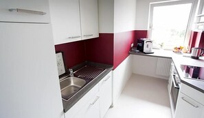 A kitchen with white cabinets, a stainless steel sink, and a window providing natural light. - Hotel Restaurant Zur Post Lohfelden (Lohfelden)