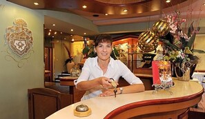 A hotel reception area with a counter, a decorative emblem on the wall, and a flower arrangement. - Hotel Restaurant Zur Post Lohfelden (Lohfelden)