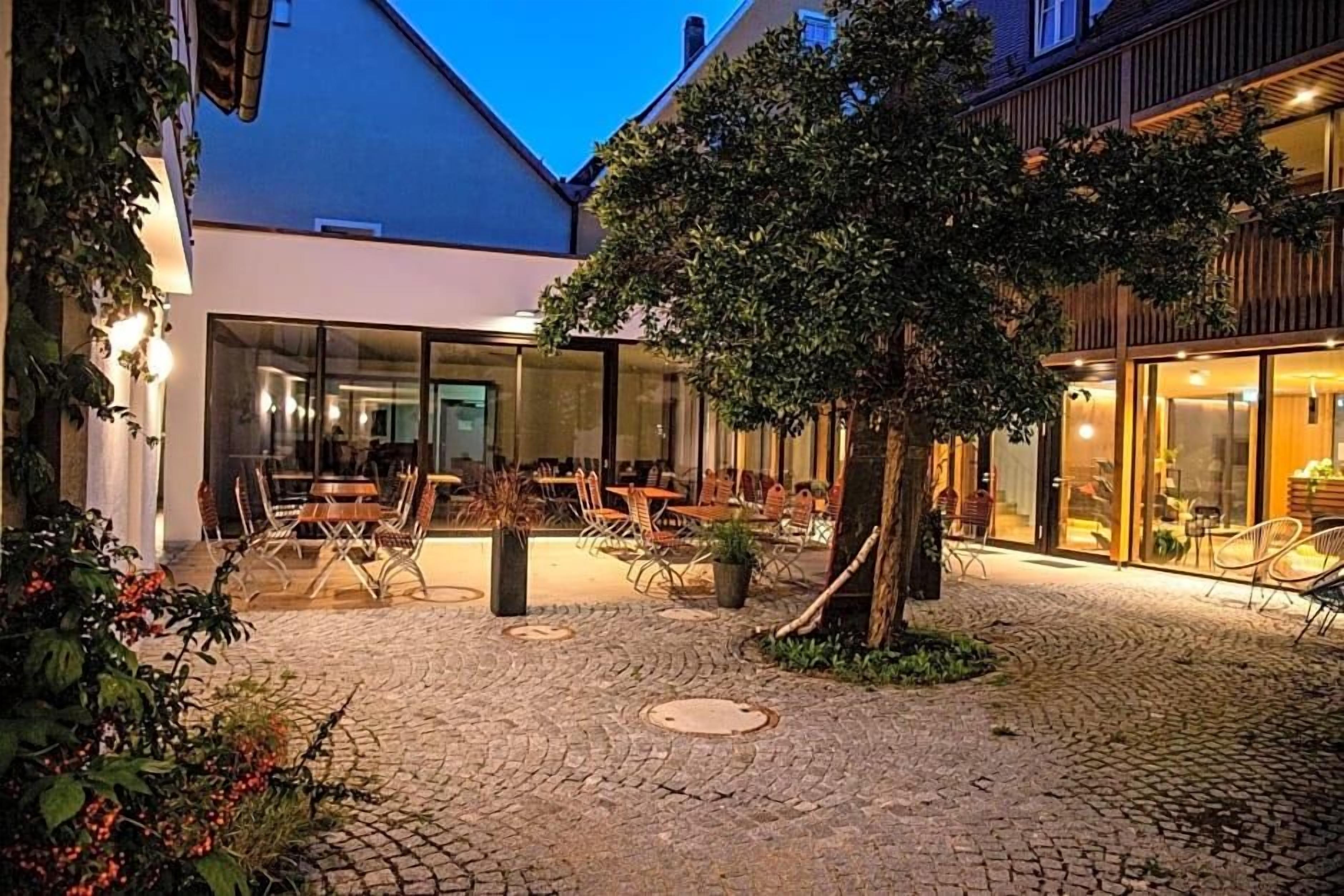An outdoor café area with tables and chairs, a cobblestone path, and a tree.