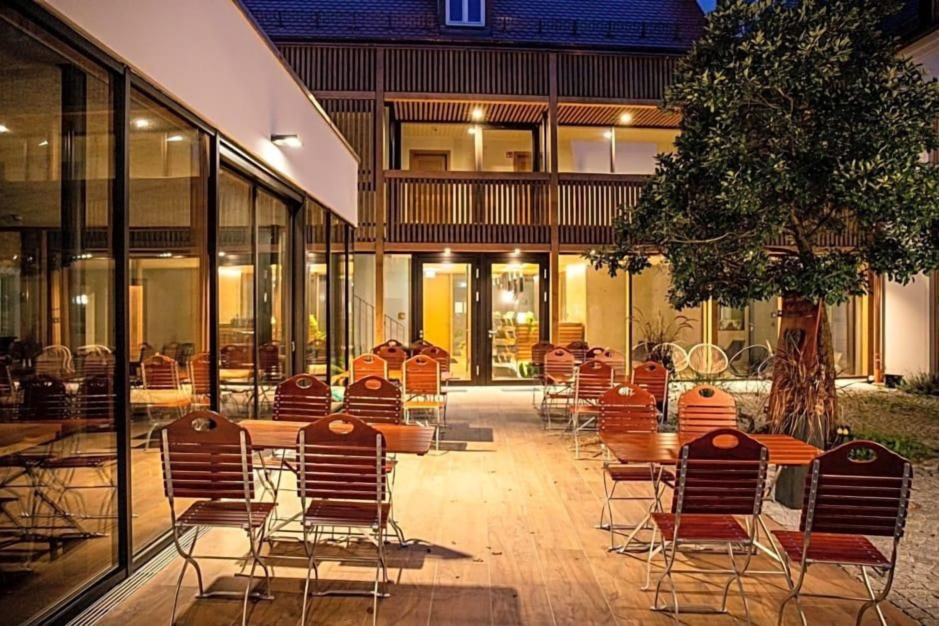 Un espacio al aire libre con mesas, sillas, un muro de cristal y una terraza de madera.