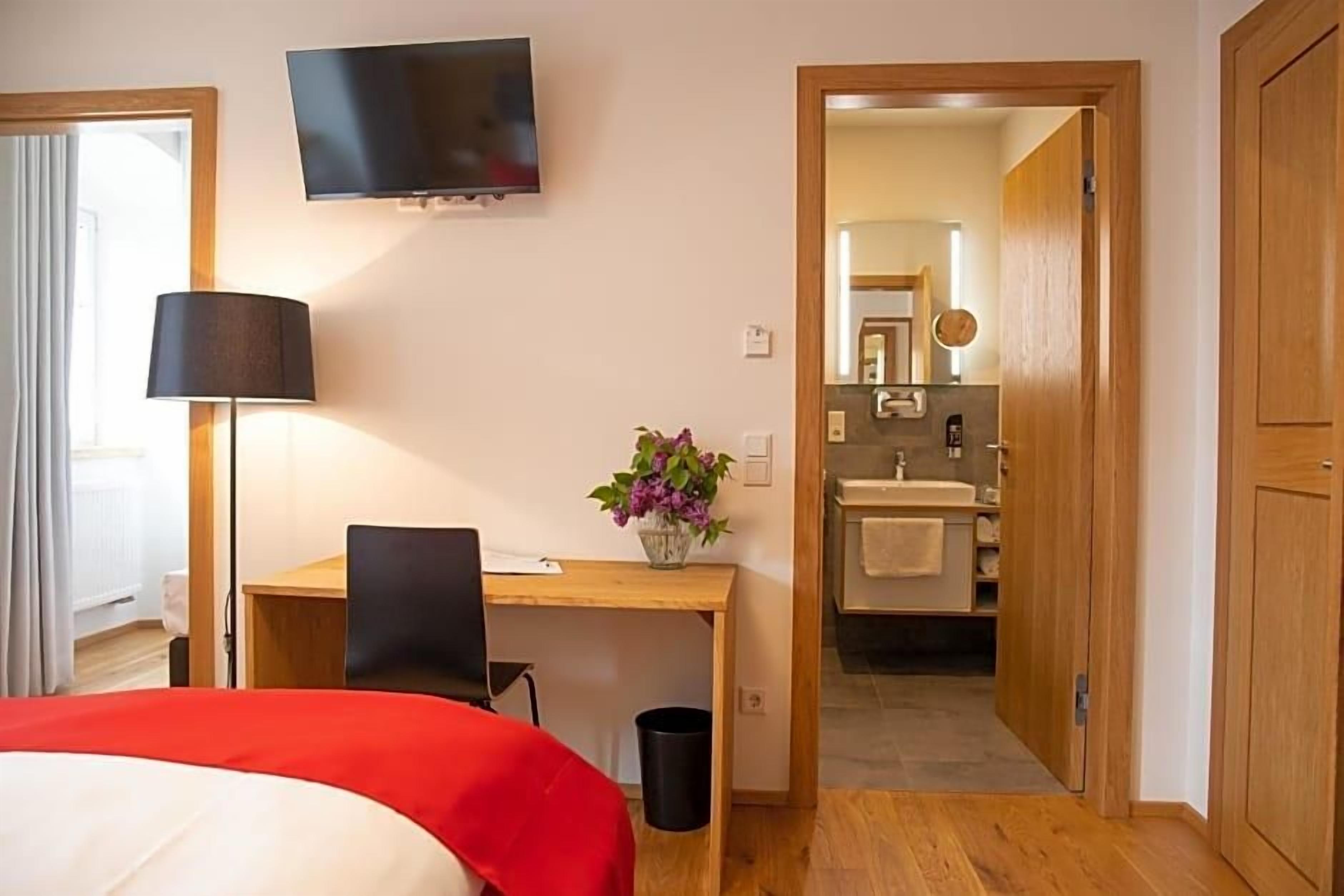 A hotel room with a bed, desk, chair, TV, and a bathroom visible through an open door.