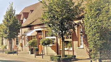 A traditional brick building with a pitched roof, a central entrance with a door, and a small tree in front.