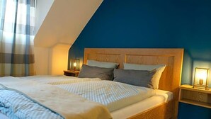 A bedroom with a sloped ceiling, a bed with a wooden headboard, two bedside tables with lamps, and a blue accent wall. - Hotel Restaurant Venner Moor (Senden)