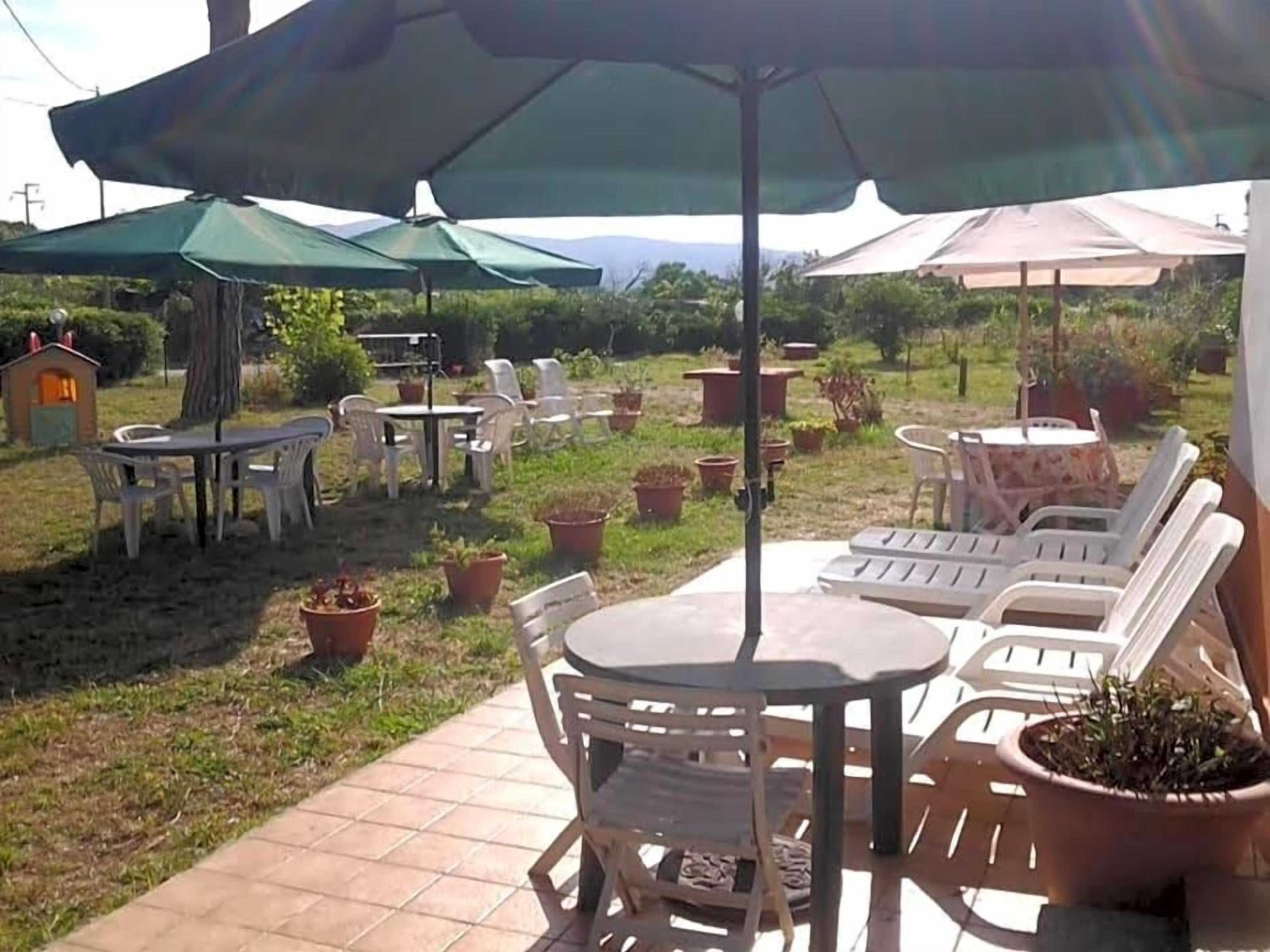 An outdoor patio area with tables and chairs, some covered by umbrellas, and potted plants.
