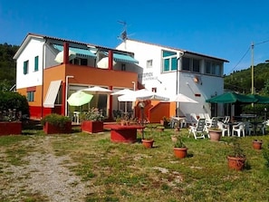A two-story building with a reception area, outdoor seating, and potted plants. - Hotel Rustichello (Campo nell'Elba)