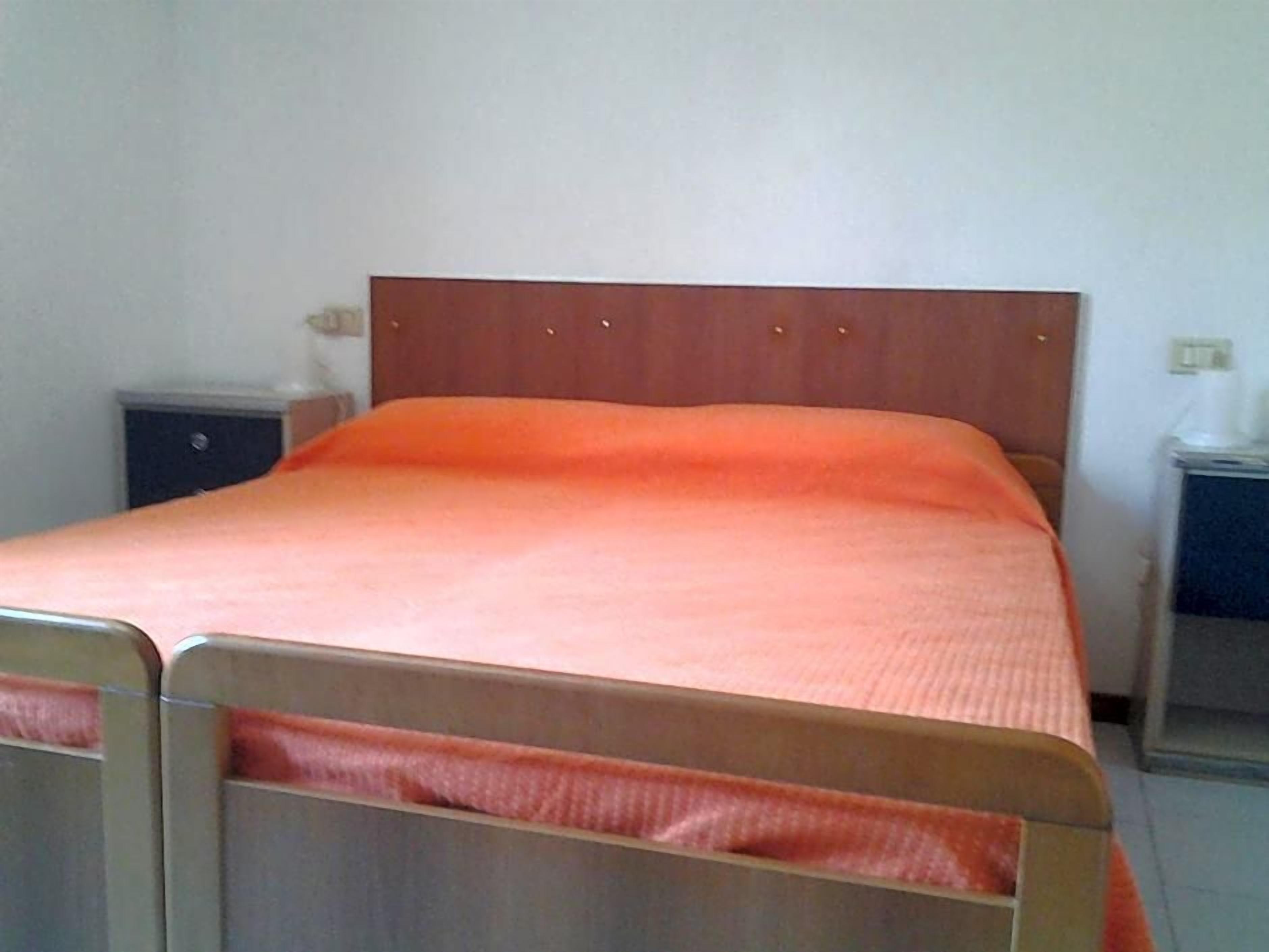 Un letto singolo con un poggiatesta in legno e copriletto arancione semplice in una stanza dalle pareti bianche.