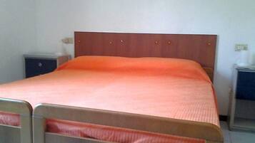 Un letto singolo con un poggiatesta in legno e copriletto arancione semplice in una stanza dalle pareti bianche.