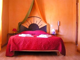 Una cama con un edredón rojo, un cabecero con un diseño similar al sol y una cortina con drapeado.