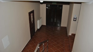 Ein Korridor mit gefliestem Boden, einem Heizkörper, einer Tür mit einem Schild und einer Handläufe.