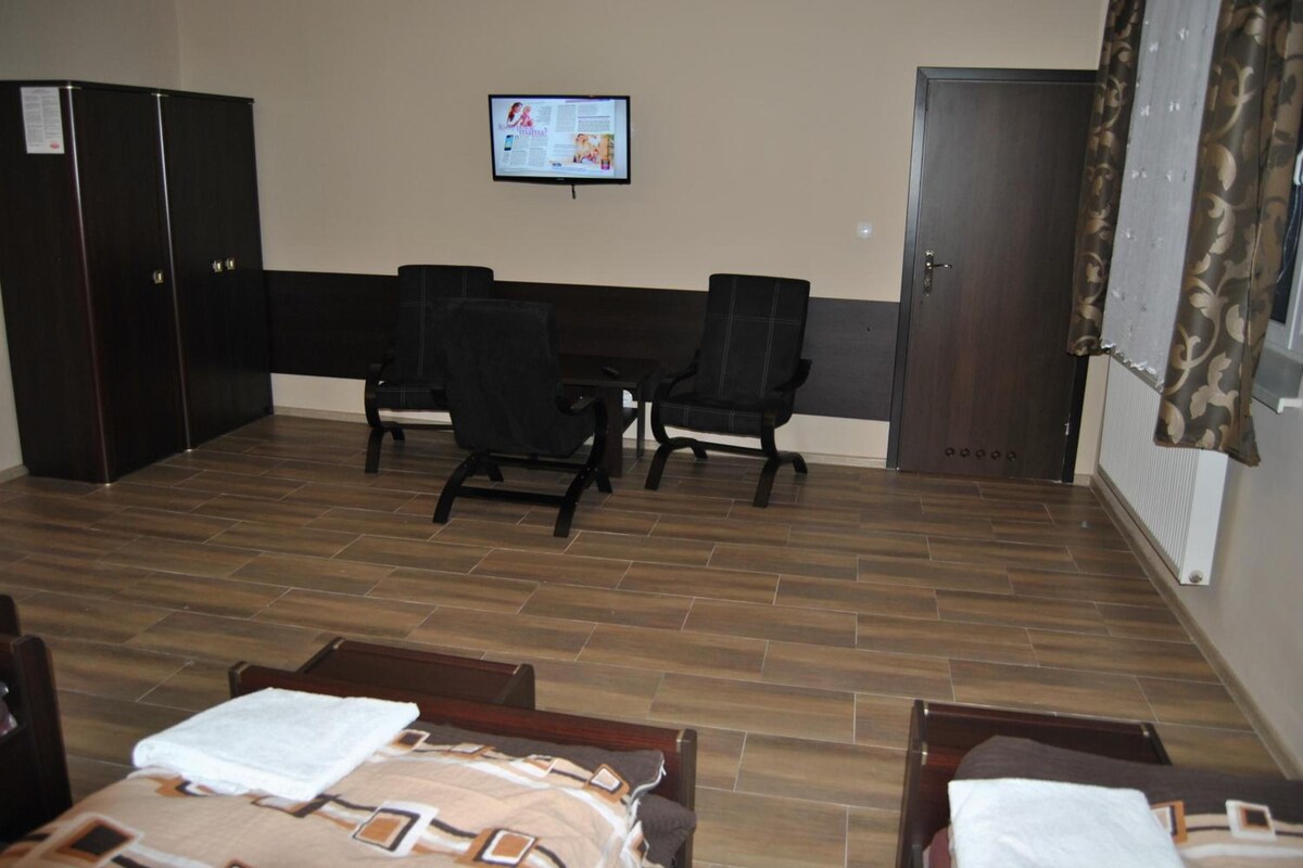 A hotel room with a bed, two chairs, a desk, and a television on the wall.