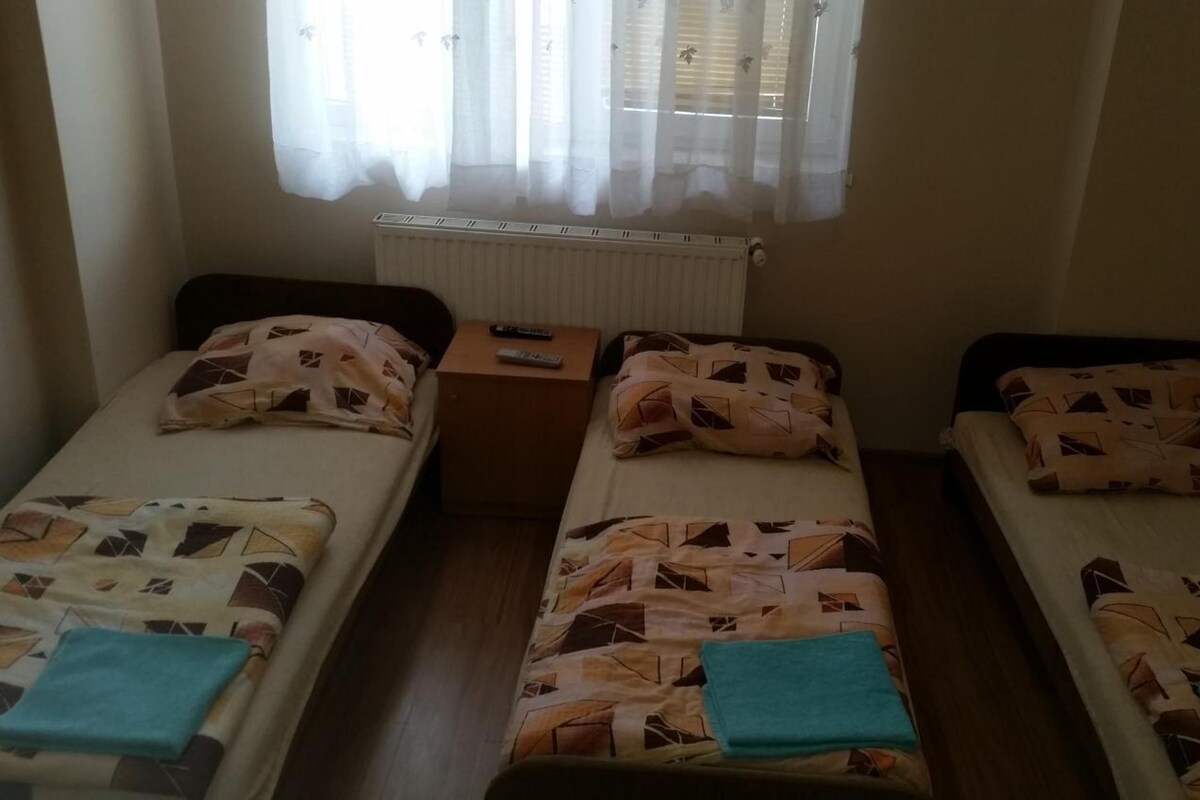 A room with three single beds, a small table, and a window with curtains.