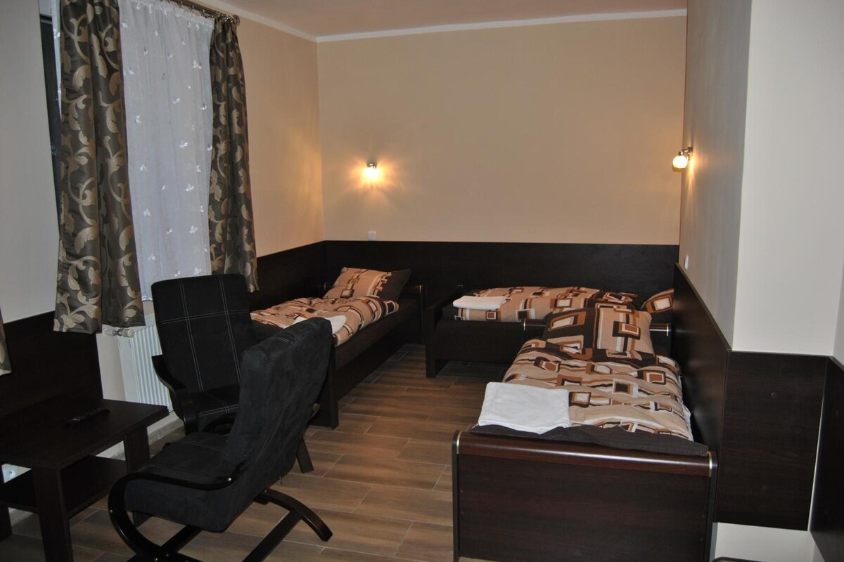 A room with a bed, a chair, and a small table. There are two wall-mounted lights.