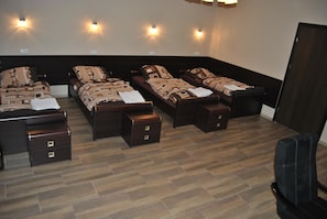 A room with four beds arranged in a semi-circle, each with a matching headboard and footboard. There are bedside tables with drawers, and the room has a wooden floor.