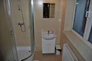 A bathroom with a glass-enclosed shower, a white sink, and a window with blinds. - Hotel Go Ociniec (Wloclawek)