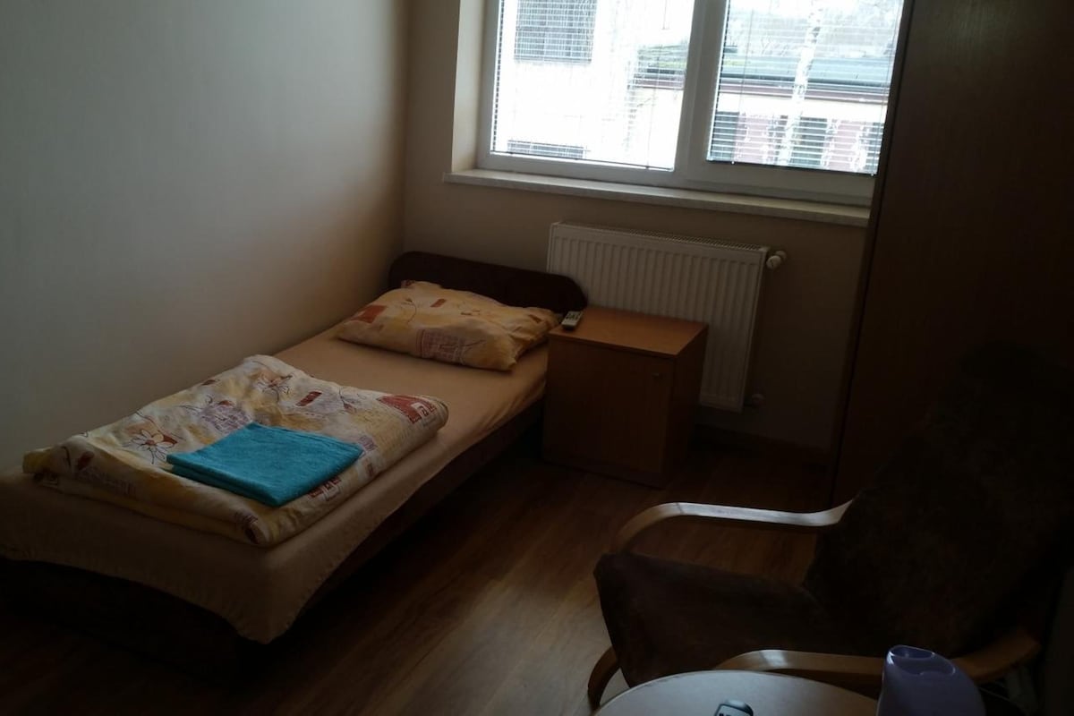 A small, single-bed room with a wooden floor, a window, and a radiator.