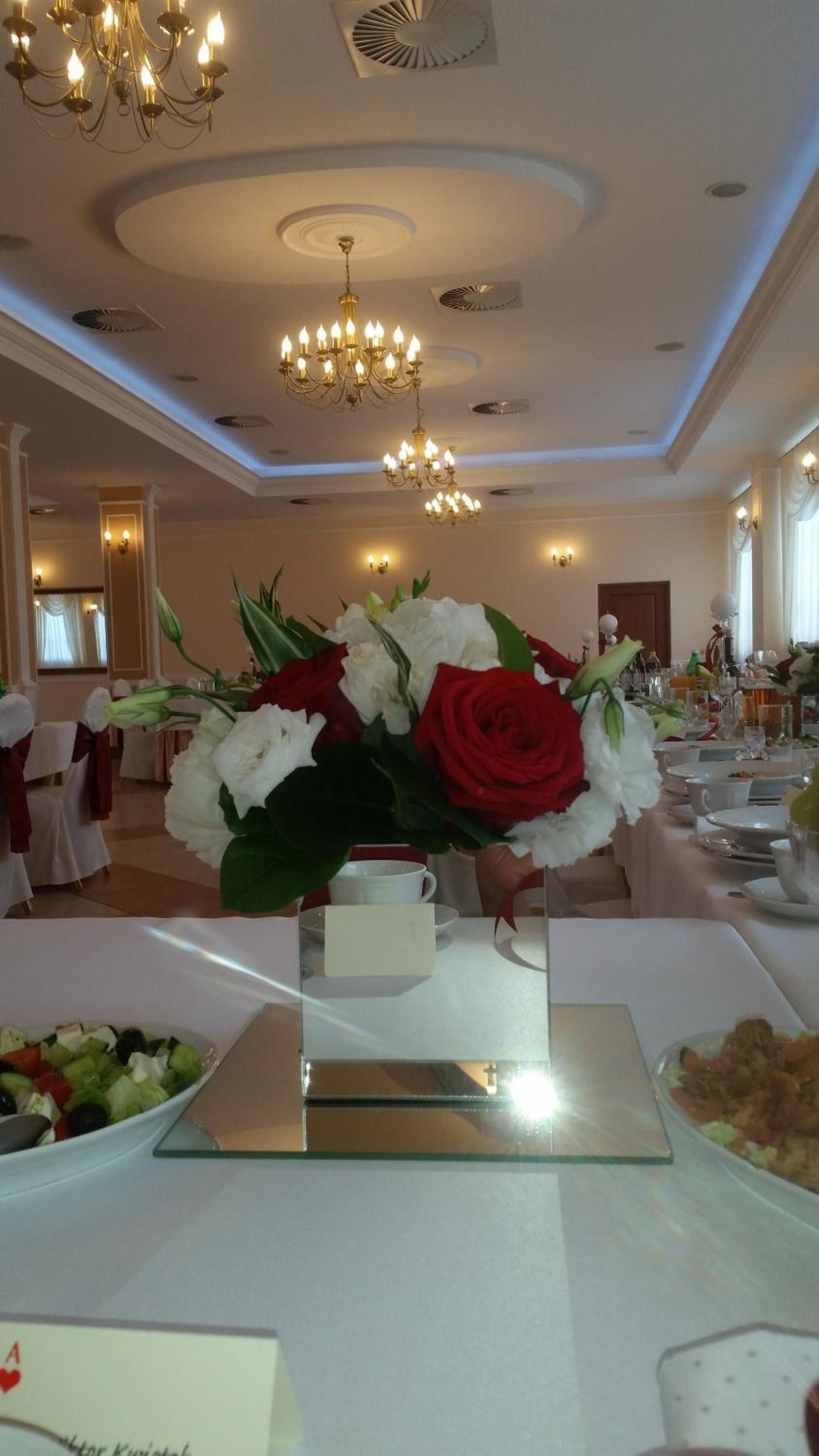 A banquet hall with round tables, floral centerpieces, and chandeliers.