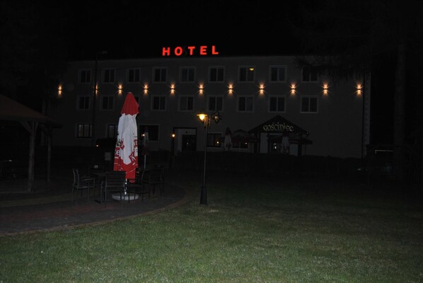 A hotel with a sign that reads 'HOTEL' above the entrance. There are outdoor tables and chairs under umbrellas.