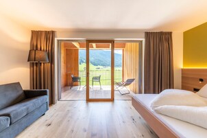 Una habitación de hotel con cama, sofá, mesa con sillas y balcón con vista a las montañas.