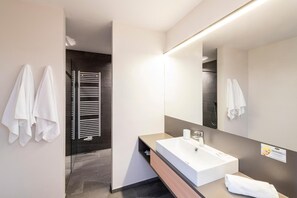 A modern bathroom with a large mirror, a white sink, and a towel rack. - Hotel Tyrol (Valle di Casies)