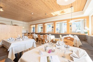 Restaurante com interiores em madeira, várias mesas preparadas para refeições e amplas janelas com vista.