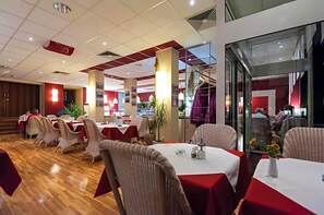 Een restaurant met meerdere tafels en stoelen, een houten vloer en een kleurenspel in rood en wit.