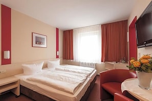 Een hotelkamer met een bed, een bureau, een stoel, een televisie en een raam met gordijnen.