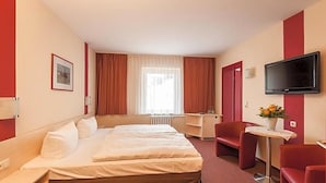 A hotel room with a bed, a desk, a chair, a television, and a window with curtains. - Panorama Hotel Bansin (Heringsdorf)