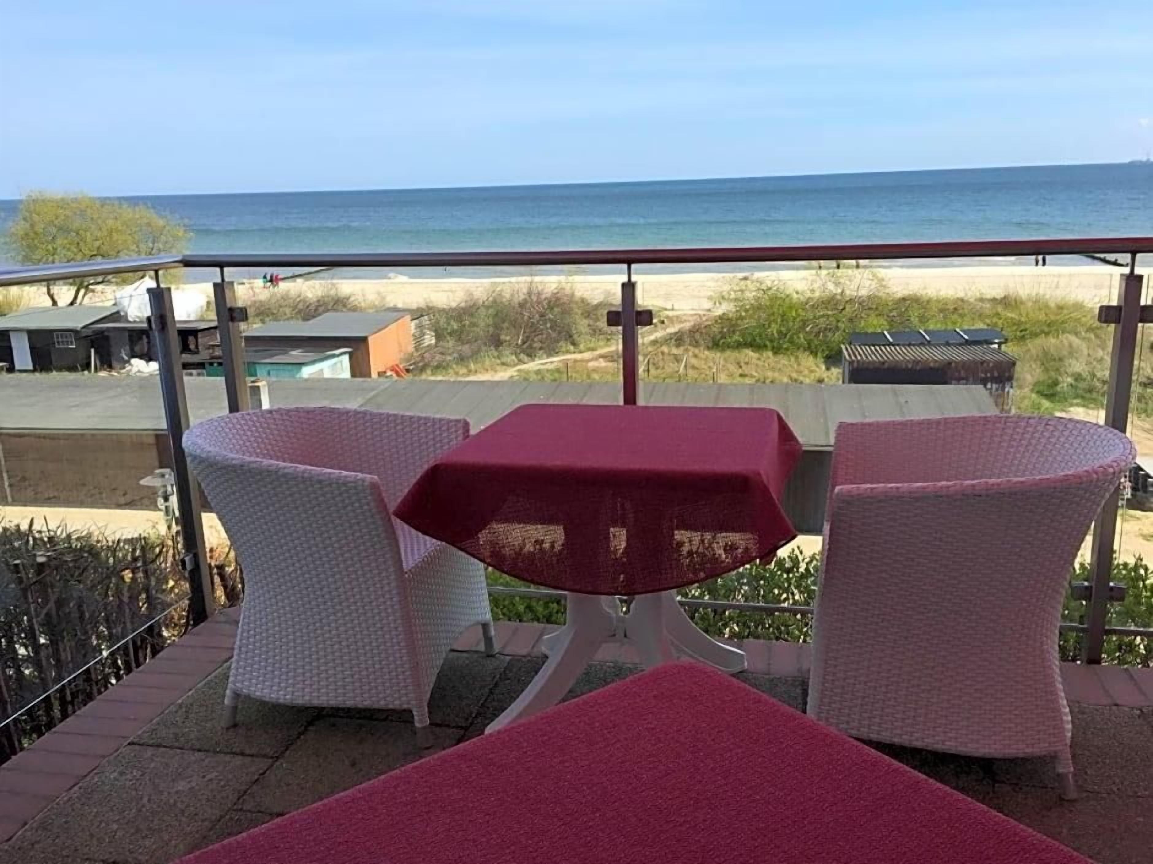 A terrace with a table and chairs, overlooking a beach and ocean.