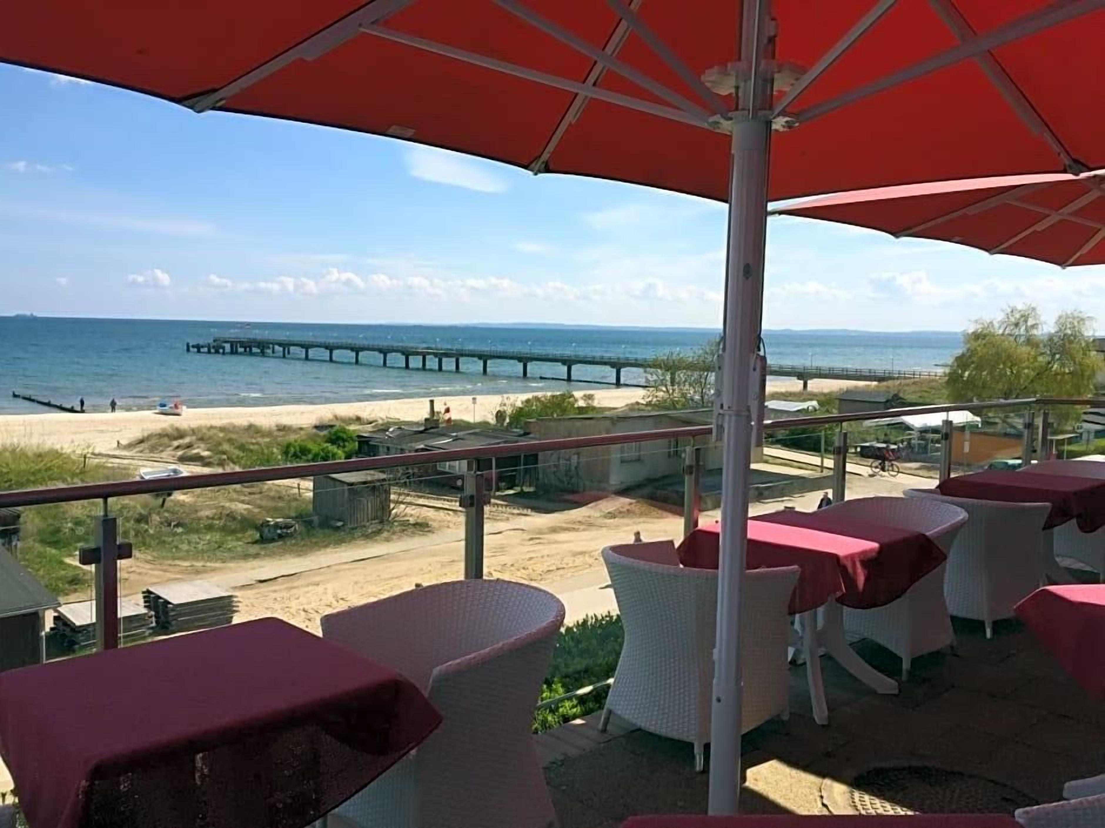 Une terrasse en bord de mer avec des tables et des chaises, une jetée en arrière-plan et un ciel dégagé.
