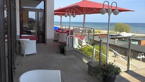 A balcony with outdoor seating, a view of the sea, and a red umbrella. - Panorama Hotel Bansin (Heringsdorf)