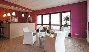 Een receptiezone met een balie, rieten stoelen, een glazen tafel en hanglampen.