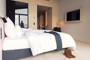 Una camera d'albergo moderna con un grande letto, una TV a muro e vista sull'esterno.