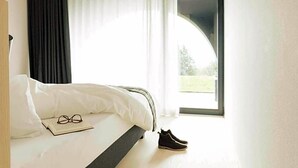 A bedroom with a bed, a pair of shoes, a pair of glasses, and a window with curtains. - Hotel Milla Montis (Rio di Pusteria)