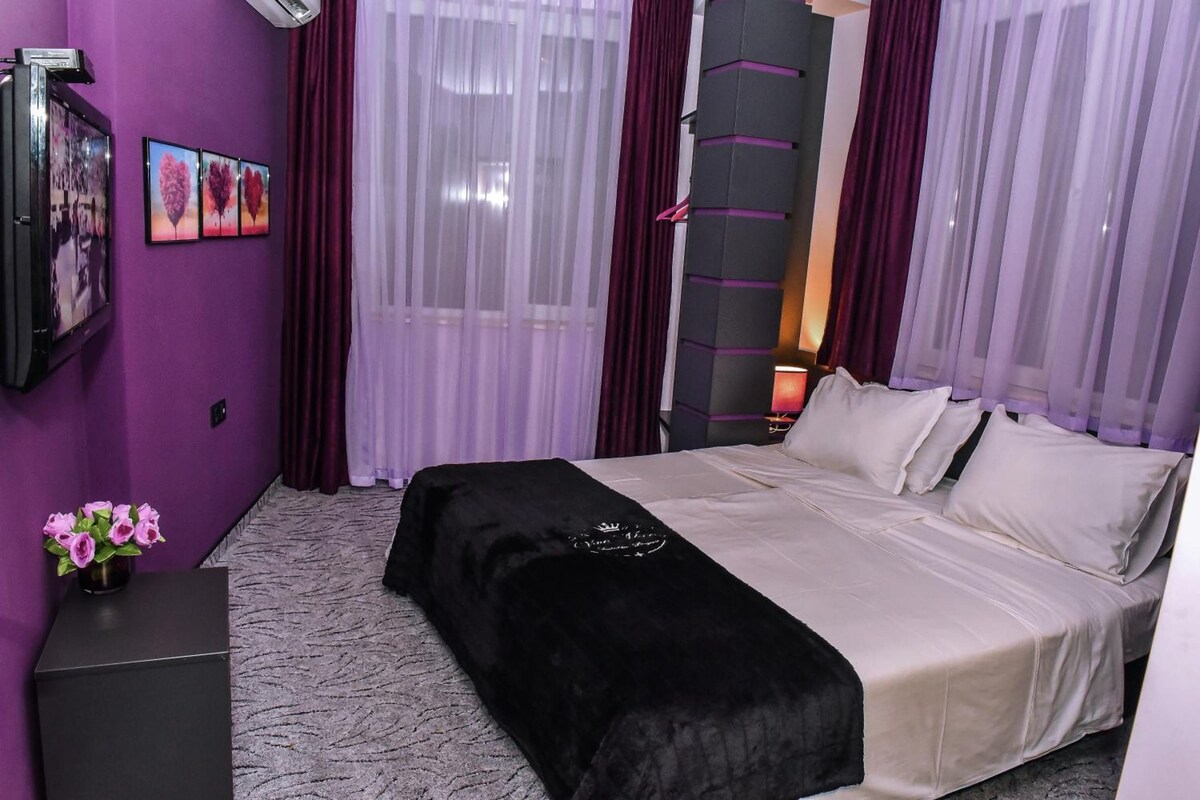 A hotel room with a bed, a desk, and a window with curtains.