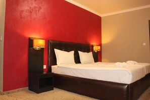 A hotel room with a large bed, two bedside lamps, and a red accent wall. - Central Guest Rooms (Asenovgrad)