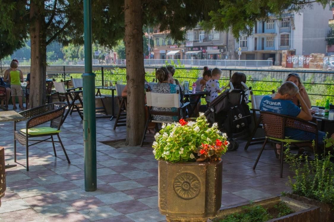 An outdoor seating area with tables and chairs, surrounded by trees and a railing.