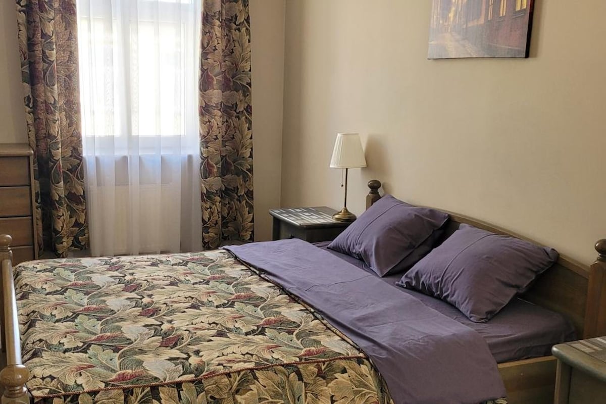 A bedroom with a bed, dresser, nightstands, lamps, and a painting on the wall.